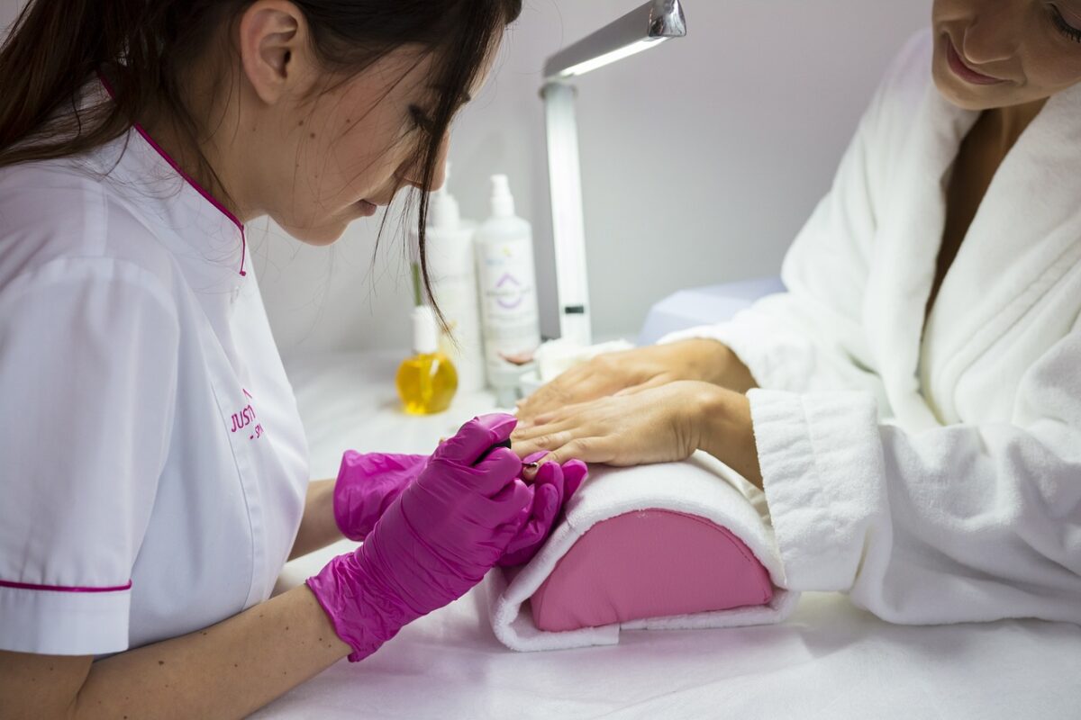 female beautician painting the nails of female customer in white bath robe